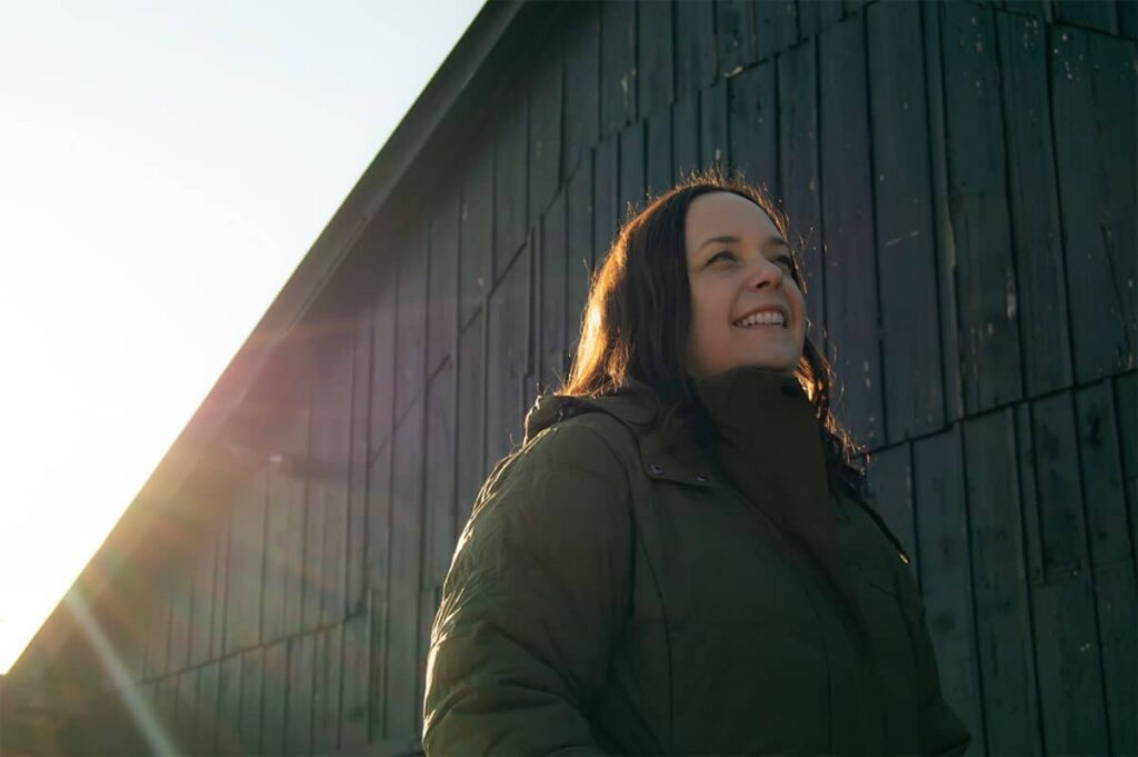 A portrait of Heidi Franklin. She has short brown hair, is wearing a green sweater, and is standing in a partially snowy field.