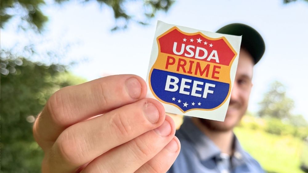 An elmwood crew member holding up the USDA Prime Beef seal.