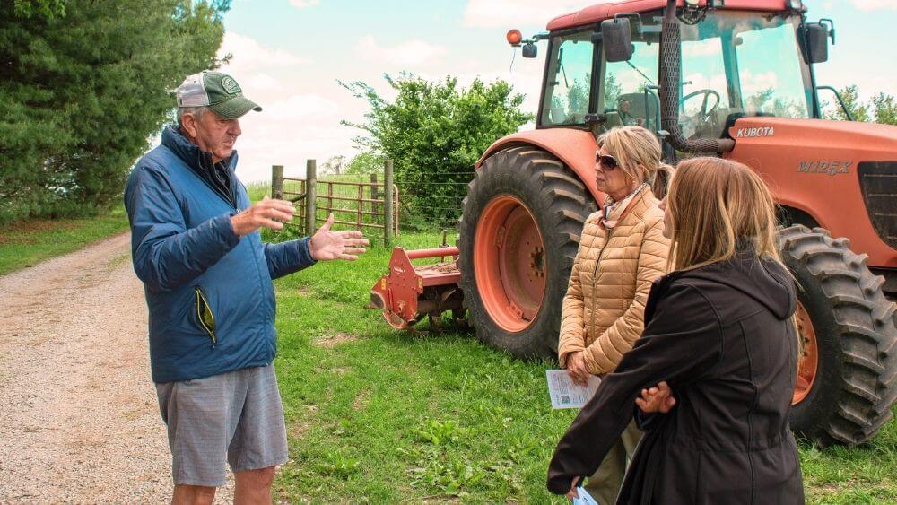 Farmer Mac talking to two farm visitors in front of a red tractor.
